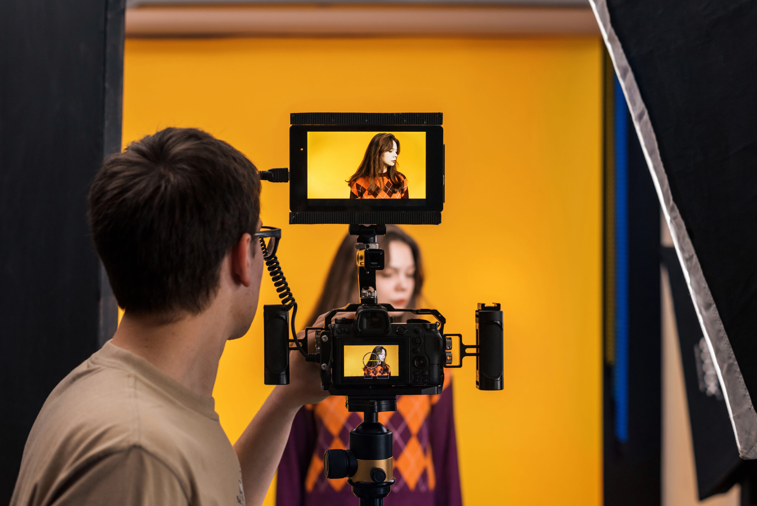 View of a professional photographer shooting a young woman using a camera with external display, yellow background